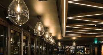 Modernes Esszimmer mit Holzbank, Holztisch, Hängelampe, großen Fenstern und Blick in den Garten, gestaltet von Brumberg.